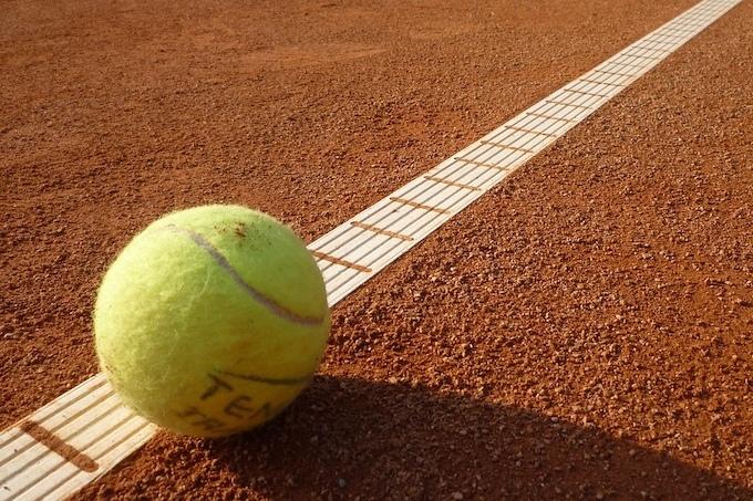 Tennisball liegt nahe an einer weißen Linie auf einem braunen Sandplatz.