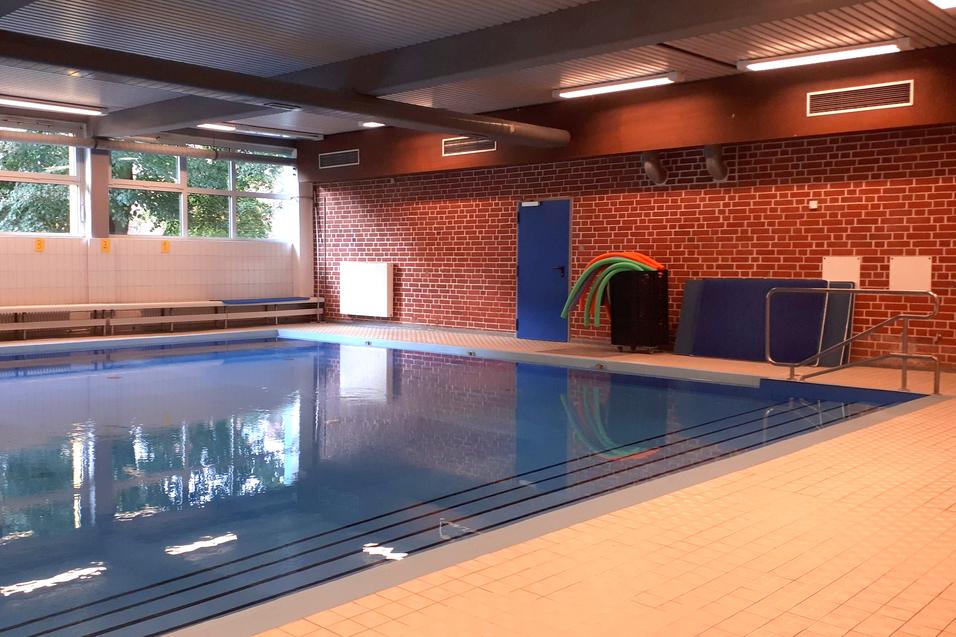 Innenansicht eines Schwimmbads mit einem leeren Wasserbecken, Tauchgeräten und Sitzbänken an der Wand.