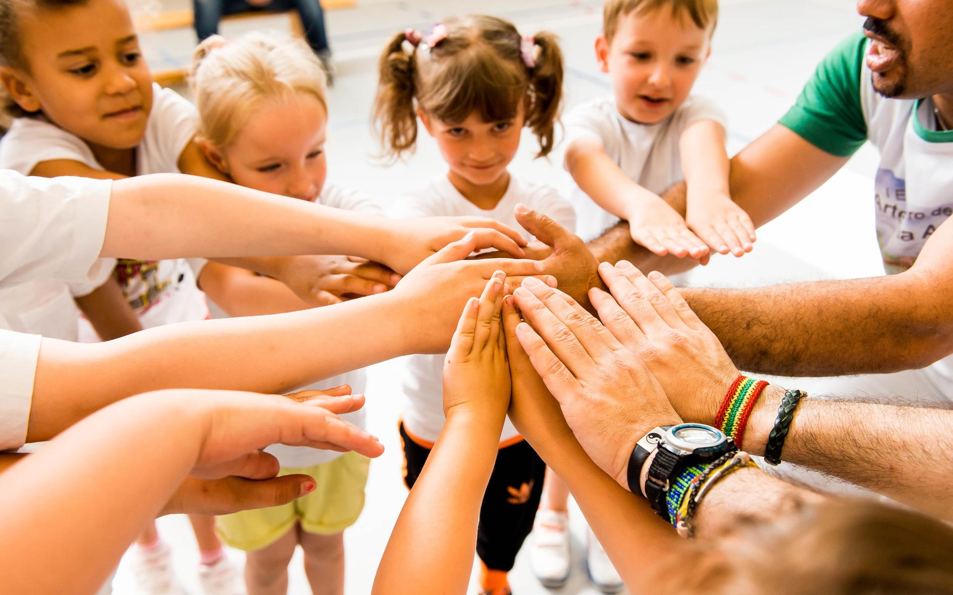 Kinder und Erwachsene legen ihre Hände in einem Kreis zusammen, symbolisieren Zusammenarbeit und Gemeinschaft.