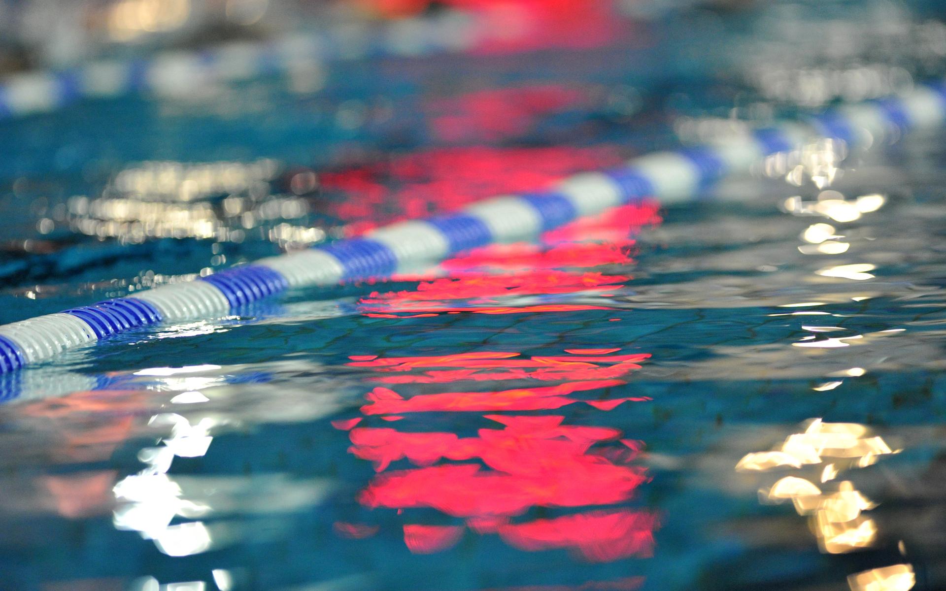 Reflektion einer blauen und weißen Schwimmbahn in klarem Wasser mit unscharfen Lichtern im Hintergrund.